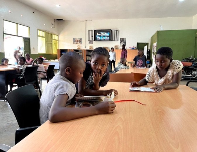 Three children reading books together at a table in KPDDI's community reading room